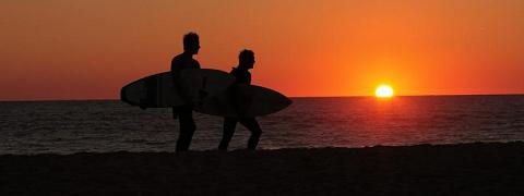 A picture of surfers walking on a beach in the sunset. By Sean Keenan