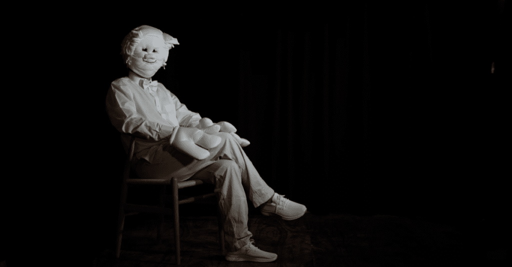 Image shows video still from Guy Oliver film, seated figure wearing mask